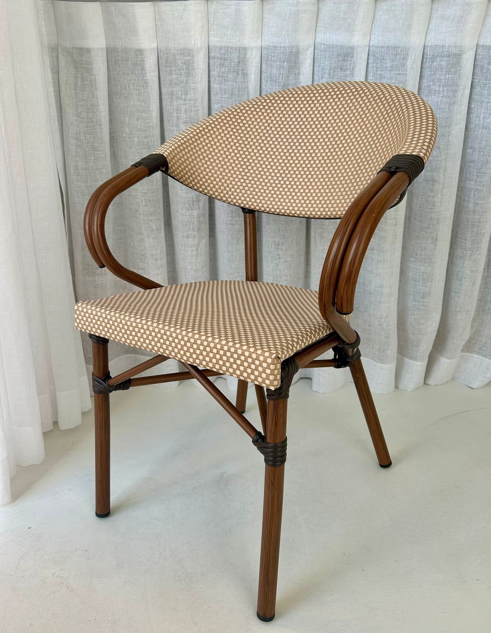 Ergonomische terrasstoel horeca outlet met ronde rug en armsteunen, afgewerkt in beige bruin wickerlook kunststof. Direct leverbaar via horeca outlet en horecameubilair outlet.