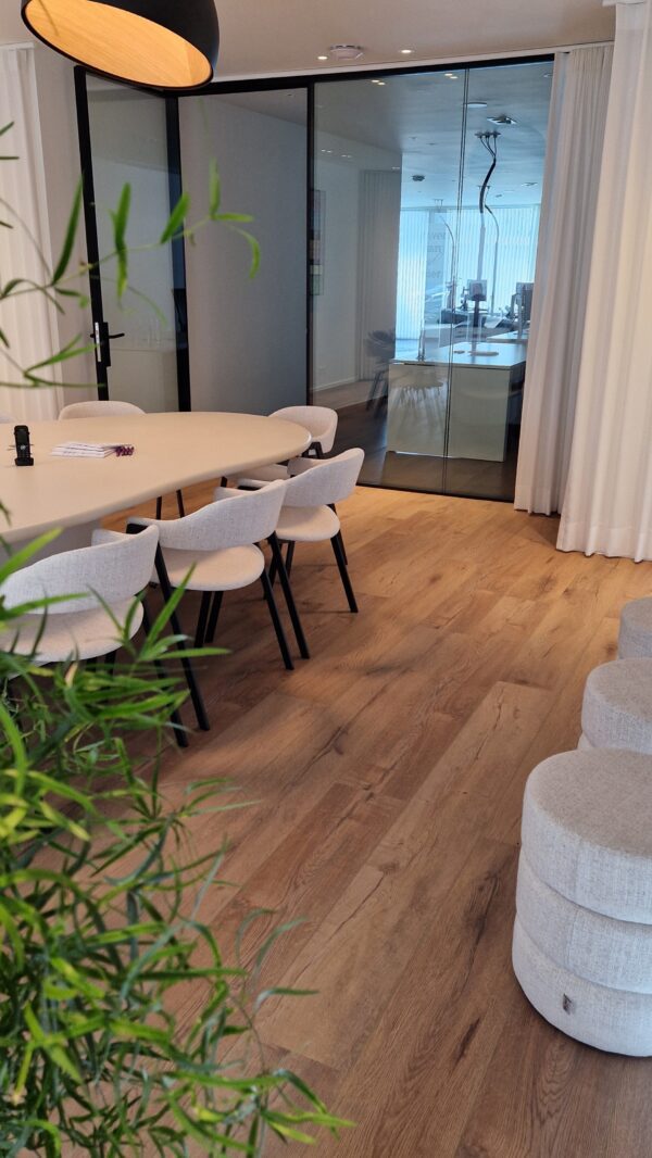 Overzicht van de vergaderruimte bij Braet & Partners (Jouw Accountant) in Gistel. Rond een ovale vergadertafel staan meerdere Nirca armstoelen, bekleed in een zachte, lichtgrijze stof met houten rug en zwart frame. Deze setting bewijst hoe meubilair van een een horeca meubel groothandel zoals Búni ook perfect past in een kantooromgeving.