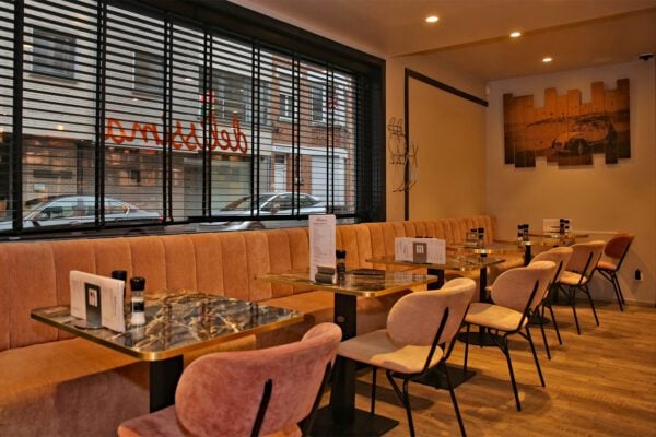 Stijlvolle horeca inrichting in Knokke-Heist met zachte roze fluwelen horeca stoelen en maatwerk wandbank in velours, gecombineerd met marmeren horeca tafels met messing afwerking. Ideaal voor een warme en comfortabele sfeer in een horecazaak.