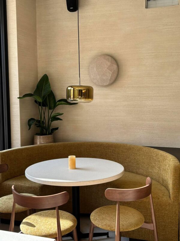 Knusse ronde hoekopstelling in Bistrobar Triple in Tielt met een op maat gemaakte ronde horeca zitbank in mosterdgeel fluweel, gecombineerd met een witte ronde tafel en stapelbare horeca stoelen in beuk met zachte beklede zitting. De warme houttinten en vilten stoeldoppen zorgen voor comfort én een akoestisch vriendelijke setting.