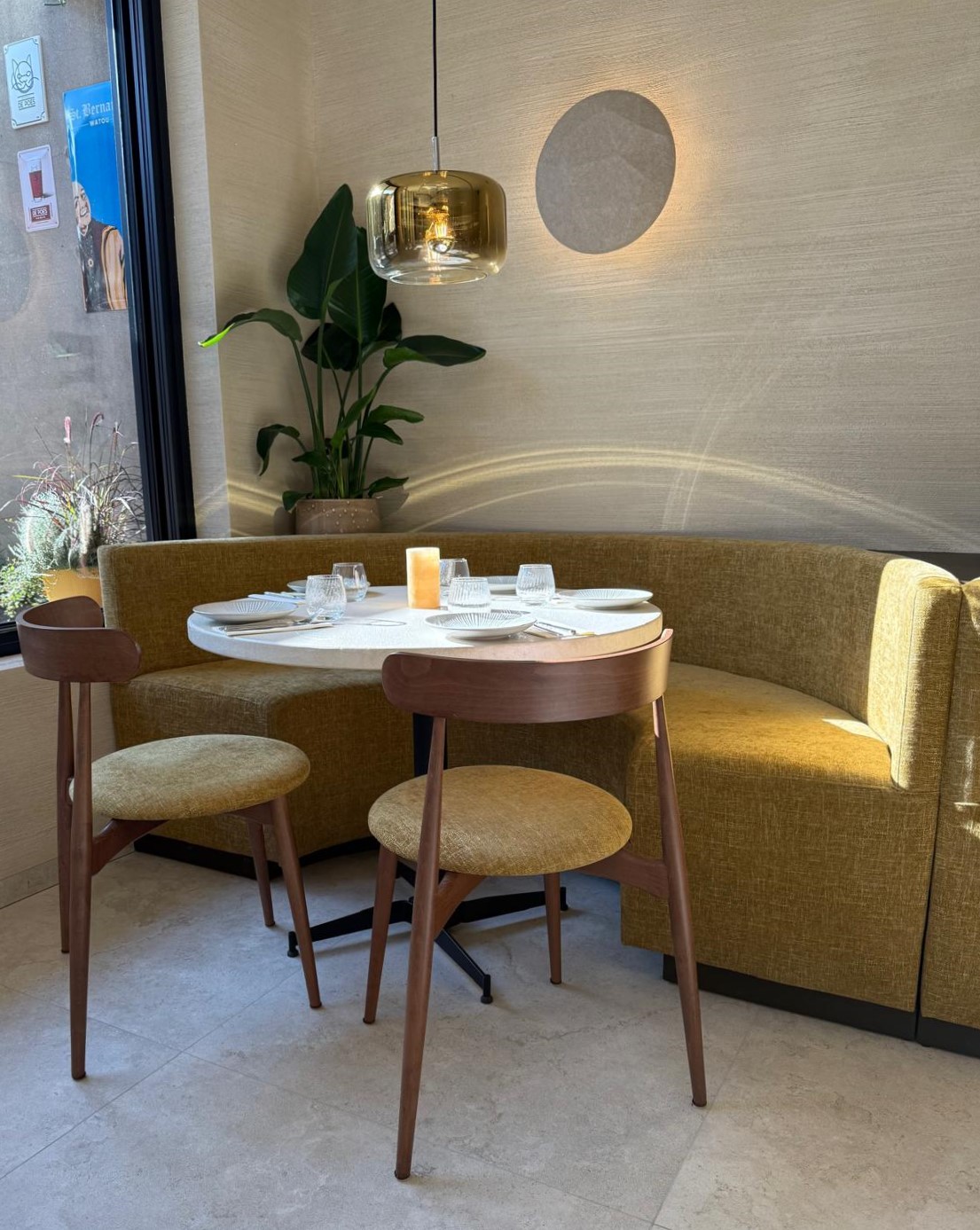 Intieme zithoek aan het raam in Bistrobar Triple, met een ronde opstelling van een fluweelzachte zitbank op maat en twee gestoffeerde horeca stoelen. Het ronde tafelblad en de gouden verlichting zorgen voor extra sfeer in deze gezellige hoek van het horeca meubilair.