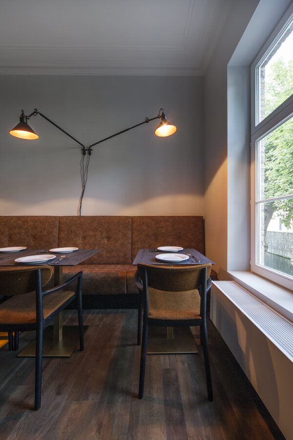 Twee compacte tafels met zwart blad, bruine gestoffeerde stoelen en een cognackleurige horeca zitbank tegen de muur. Perfect voor een intieme horecazaak inrichting met warme horeca meubels.
