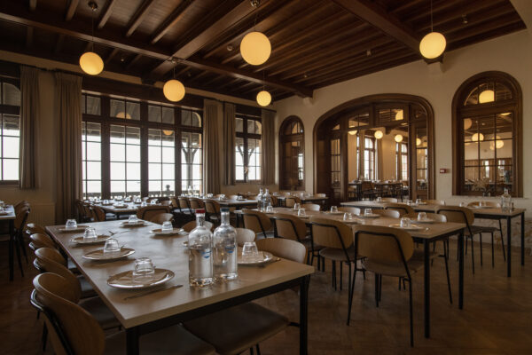 Restaurantinterieur met houten wandpanelen, lange tafels en moderne stoelen onder sfeervolle bolvormige verlichting.