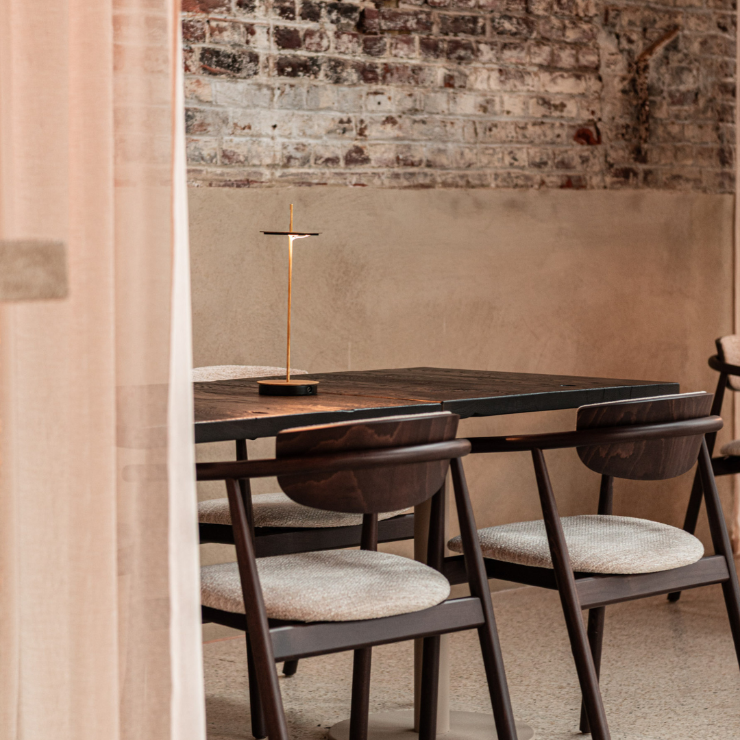 Overzicht van modern restaurant met donkere plafonds, bakstenen muren, transparante gordijnen en mix van ronde en rechthoekige tafels.