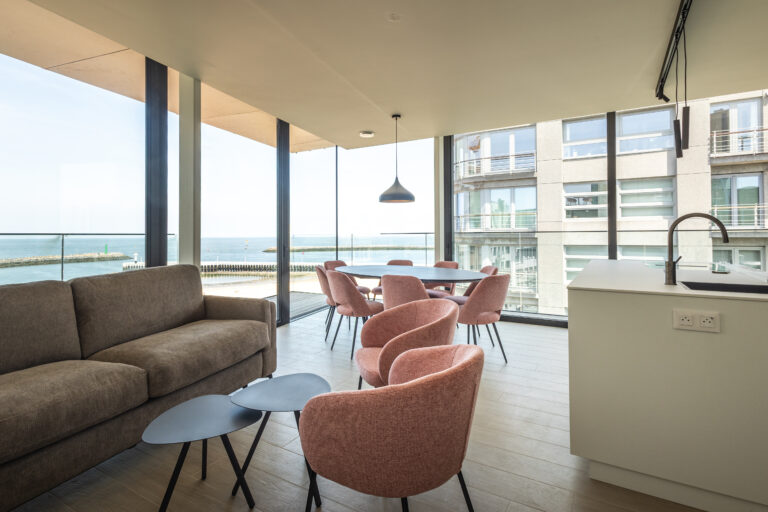 Open keuken met kookeiland en ronde eettafel, grote raampartijen met uitzicht op zee en strand