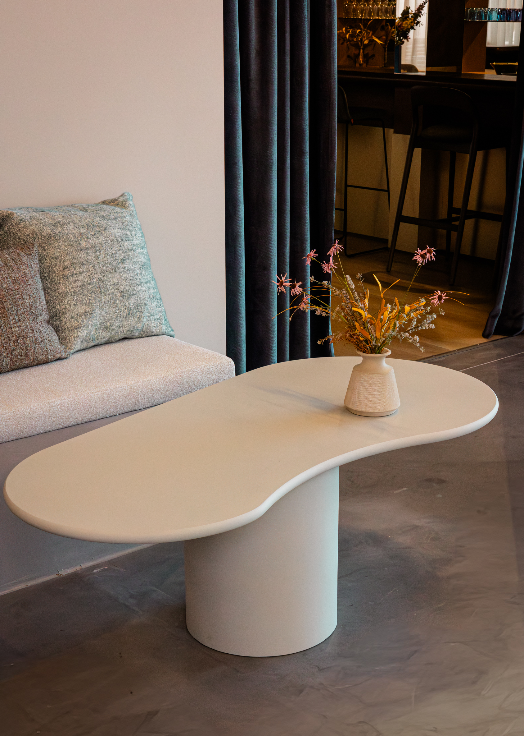 Witte organisch gevormde loungetafel Taillora met afgerond tafelblad en cilindervormige voet in een modern interieur.