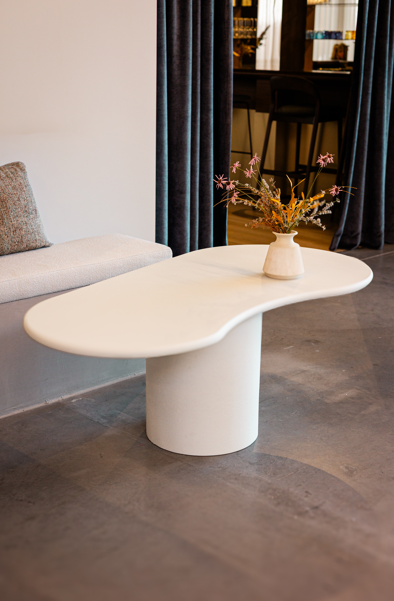 Witte organisch gevormde loungetafel Taillora met afgerond tafelblad en cilindervormige voet in een modern interieur.