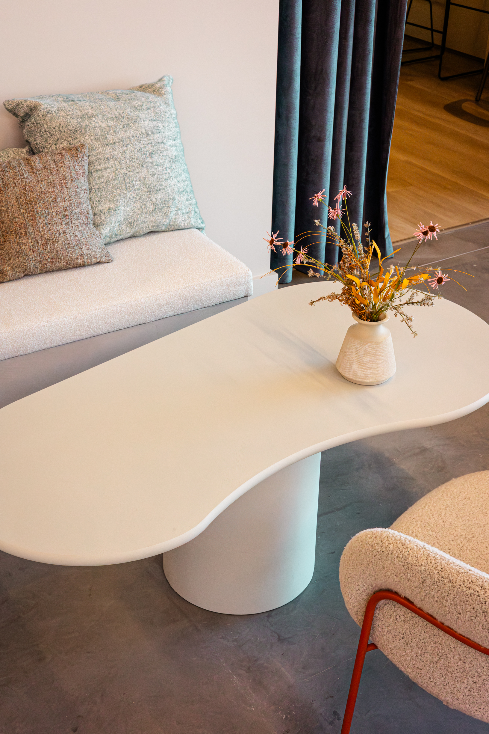 Witte organisch gevormde loungetafel Taillora met afgerond tafelblad en cilindervormige voet in een modern interieur.